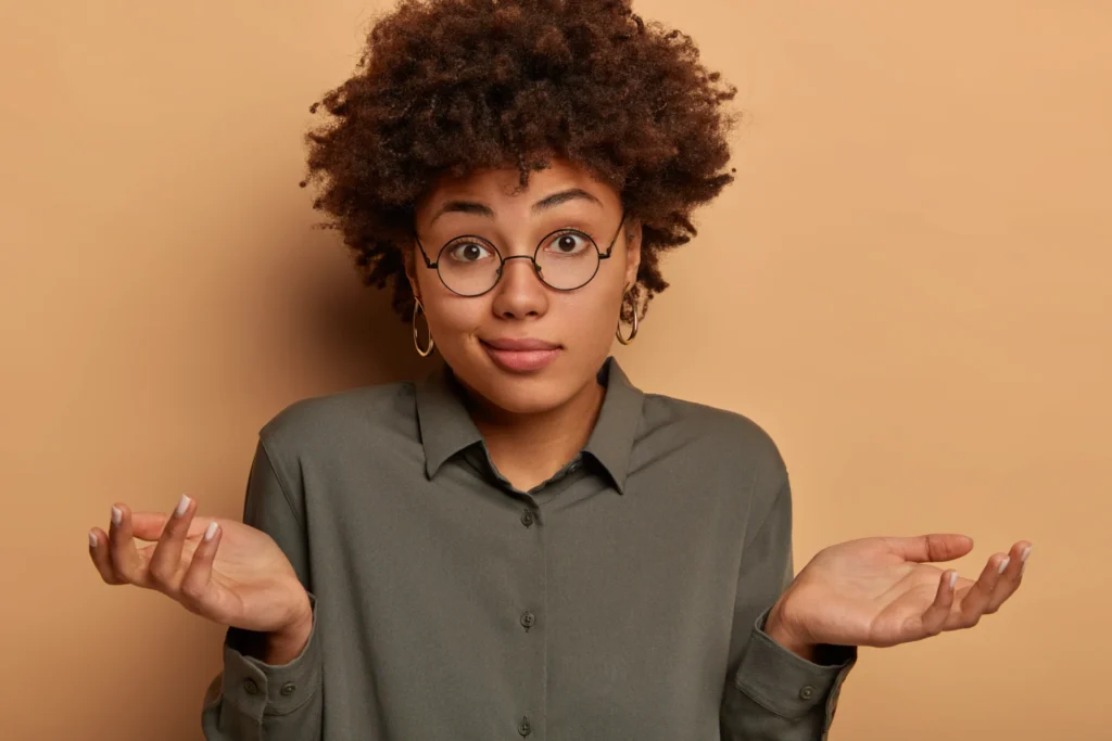 A hesitant woman shrugging her shoulders, wearing a stylish shirt and big glasses, symbolizing uncertainty and doubts.