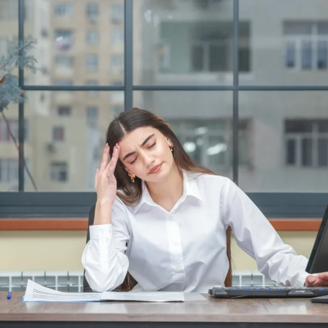 Portrait of a young businesswoman sitting at her desk, looking tired and overwhelmed.